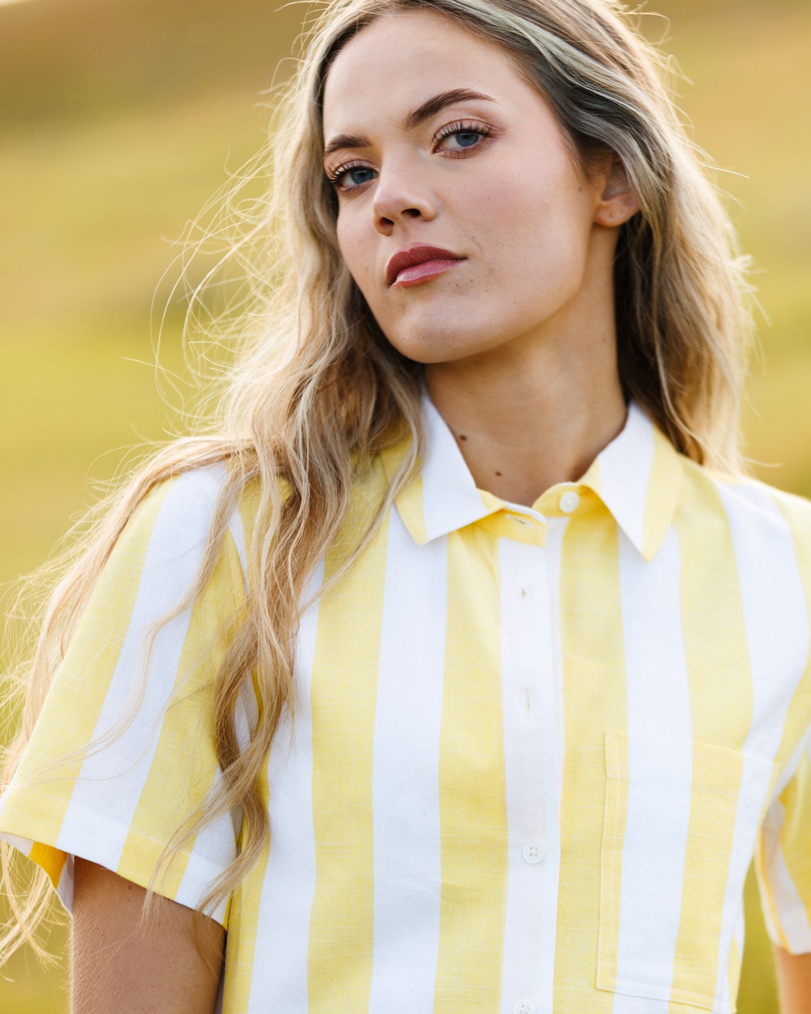 Woman wearing a yellow and white striped top sitting in a field