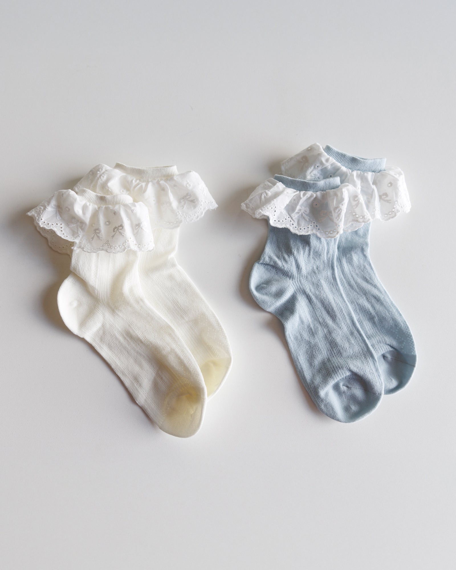Two pairs of baby socks with ruffled edges on a light gray background