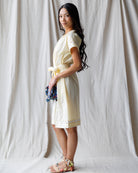 Woman in a light-colored dress standing against a plain background