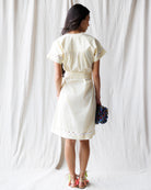 Woman wearing a white dress holding flowers against a white curtain background
