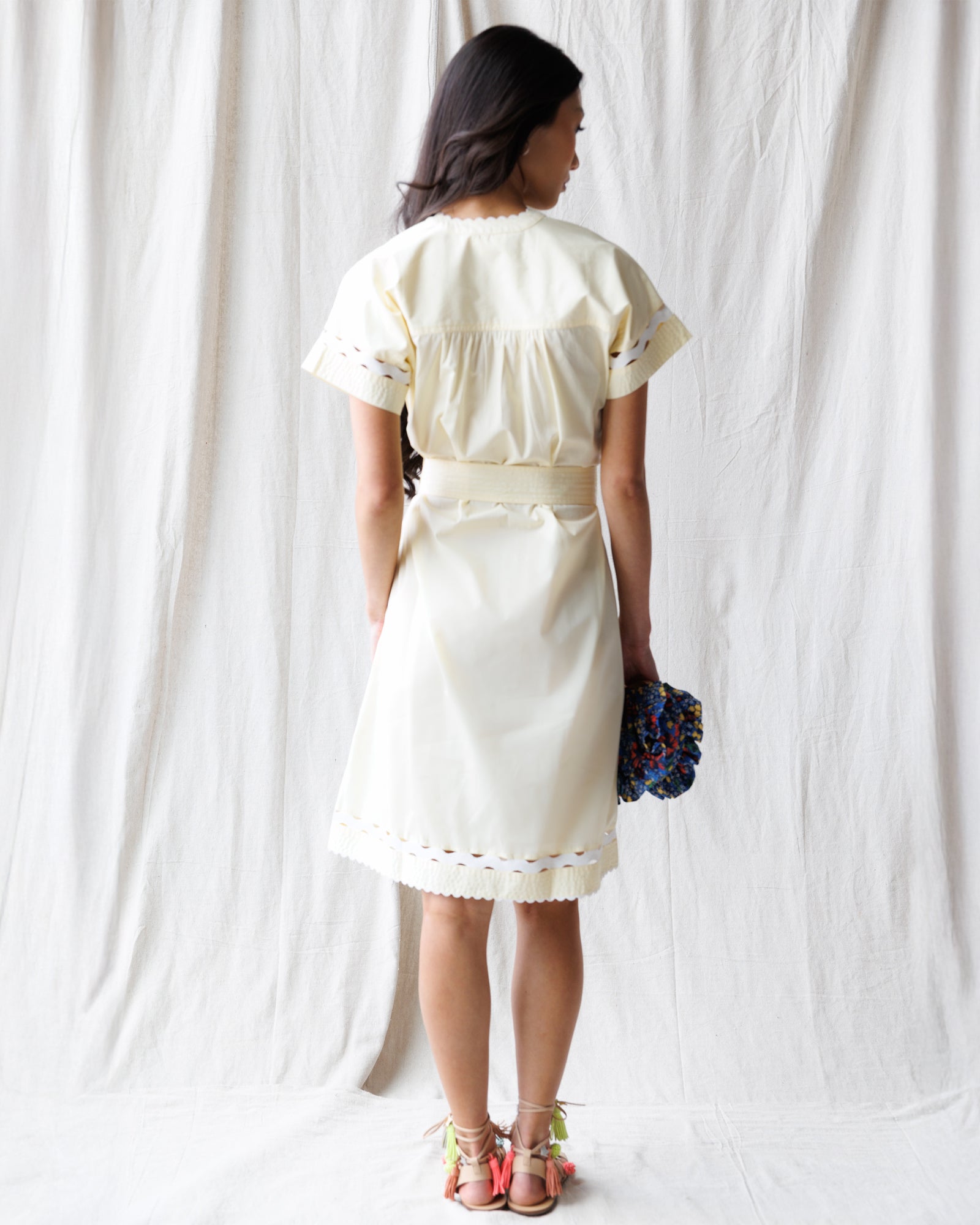 Woman wearing a white dress holding flowers against a white curtain background