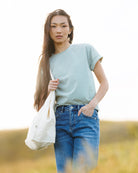 Woman wearing a striped t-shirt and jeans in a field and holding a bag