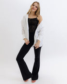 Woman wearing a white cardigan over a black top and pants on a white background