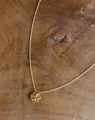 A delicate gold chain necklace with a small rose-shaped pendant, displayed on a rustic wooden surface.