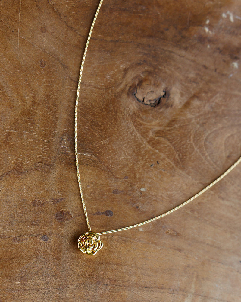 A delicate gold chain necklace with a small rose-shaped pendant, displayed on a rustic wooden surface.