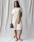 Woman wearing a white dress with lace details against a plain background