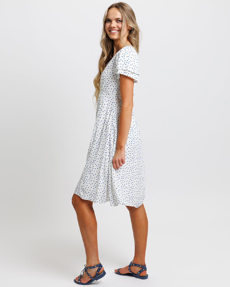 Model wearing a white with blue polka dots short sleeve v-neck midi dress