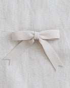 A light beige ribbed fabric ribbon tied into a neat bow, displayed on a textured linen background.