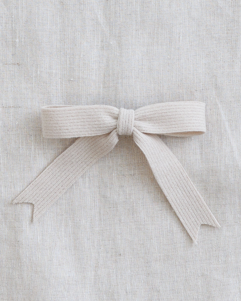 A light beige ribbed fabric ribbon tied into a neat bow, displayed on a textured linen background.