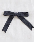 A dark charcoal gray textured fabric bow, neatly tied and displayed flat against a light beige linen background.