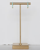 Gold T-shaped earring stand with turquoise earrings on a light gray background