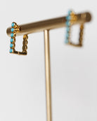 Gold earring stand with turquoise stones on a white background