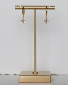 Gold hoop earrings on a gold T-shaped stand against a light gray background