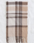 A folded plaid scarf in beige, brown, and white, displayed flat against a white fabric background.