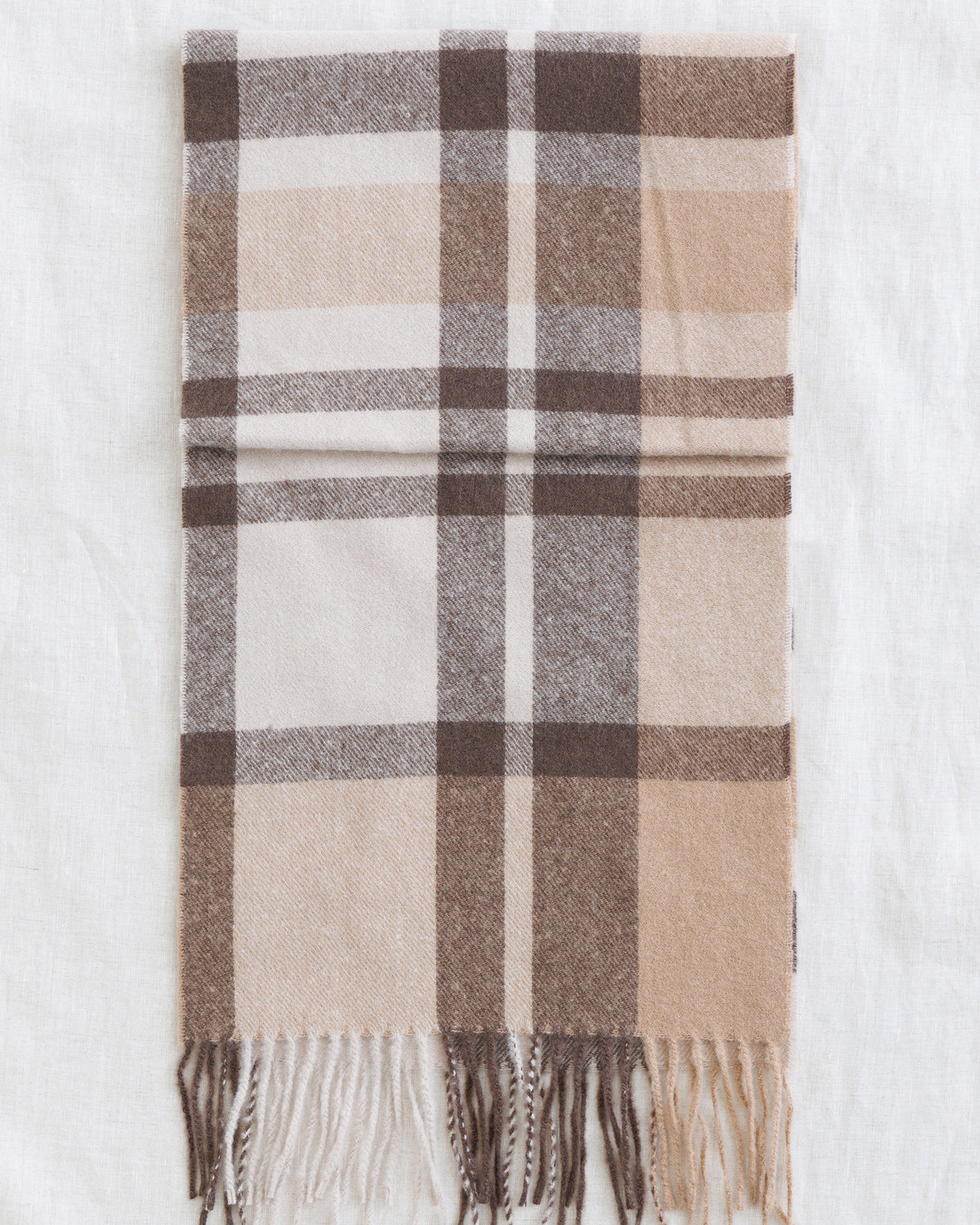 A folded plaid scarf in beige, brown, and white, displayed flat against a white fabric background.