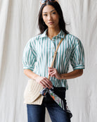 Woman wearing a green and white striped shirt with a beige bag against a white background