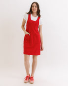Woman wearing a red pinafore dress with a white shirt underneath on a white background