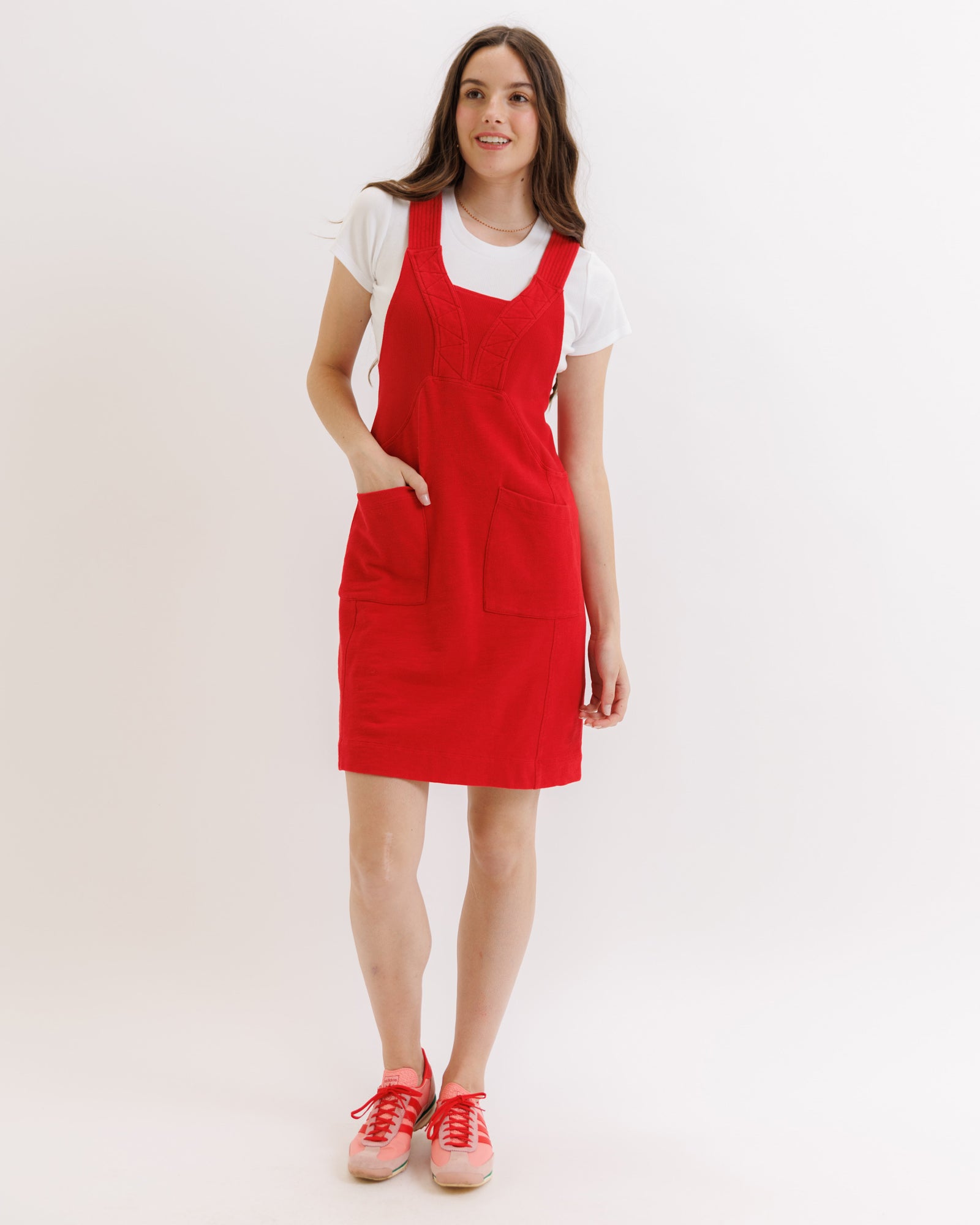 Woman wearing a red pinafore dress with a white shirt underneath on a white background