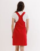 Person wearing a red pinafore dress over a white shirt on a plain background