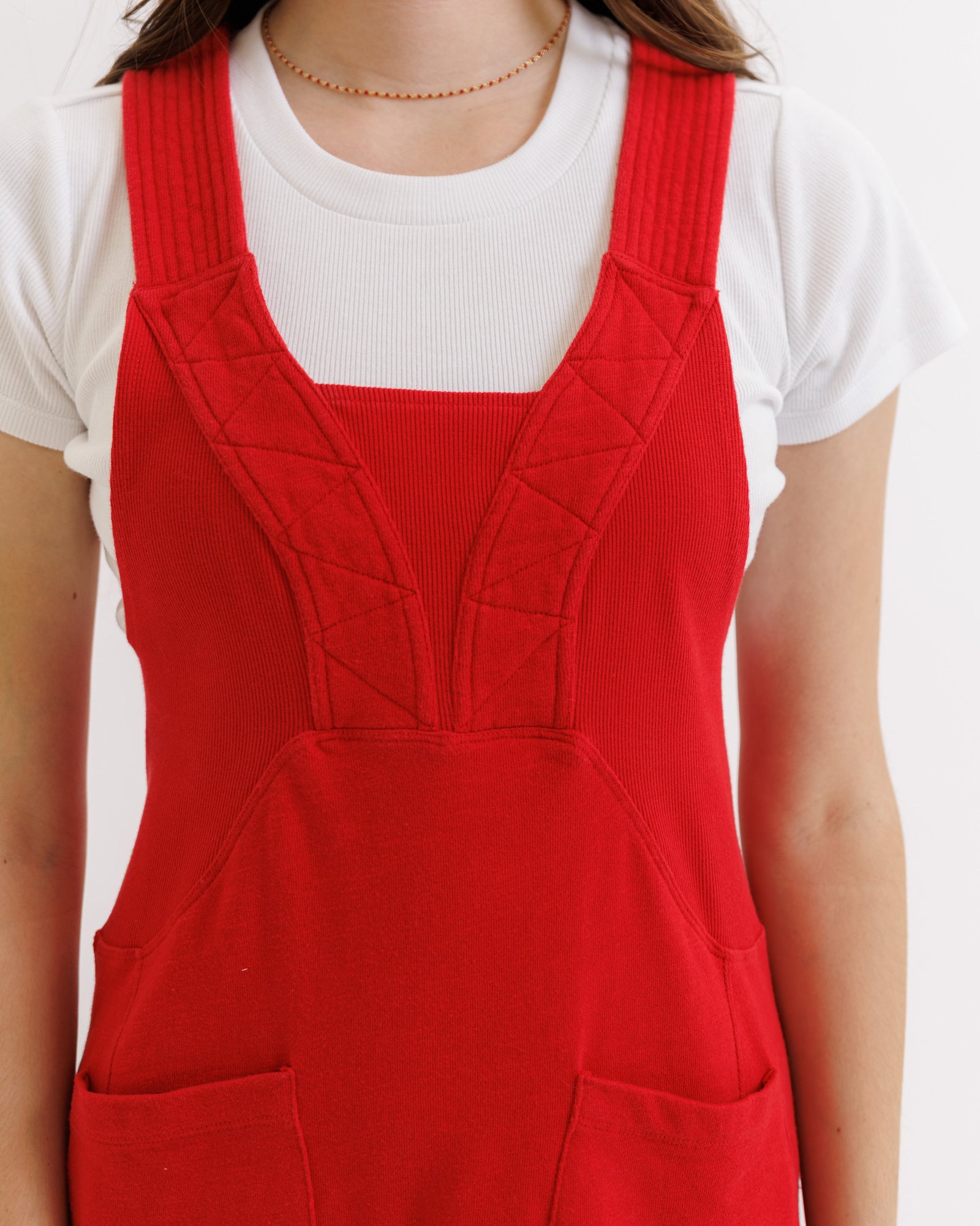 Red overall dress over a white shirt on a plain background