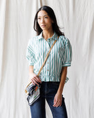 Woman wearing a green and white striped shirt with a crossbody bag against a white background