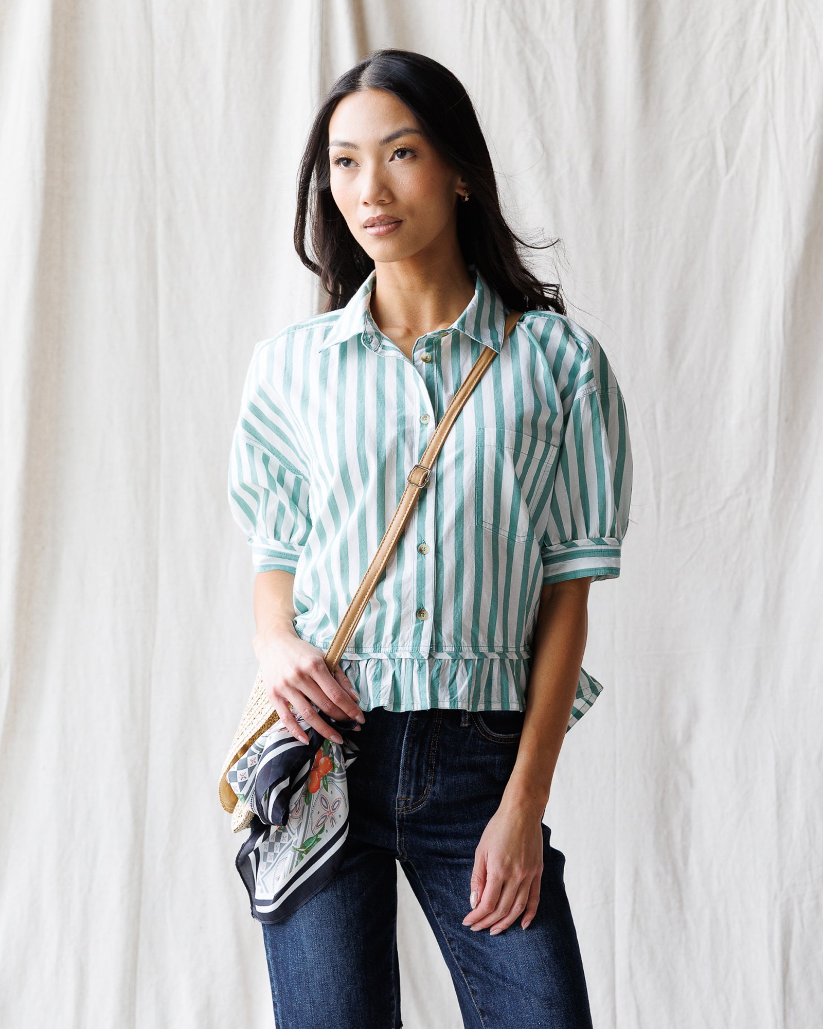 Woman wearing a green and white striped shirt with a crossbody bag against a white background