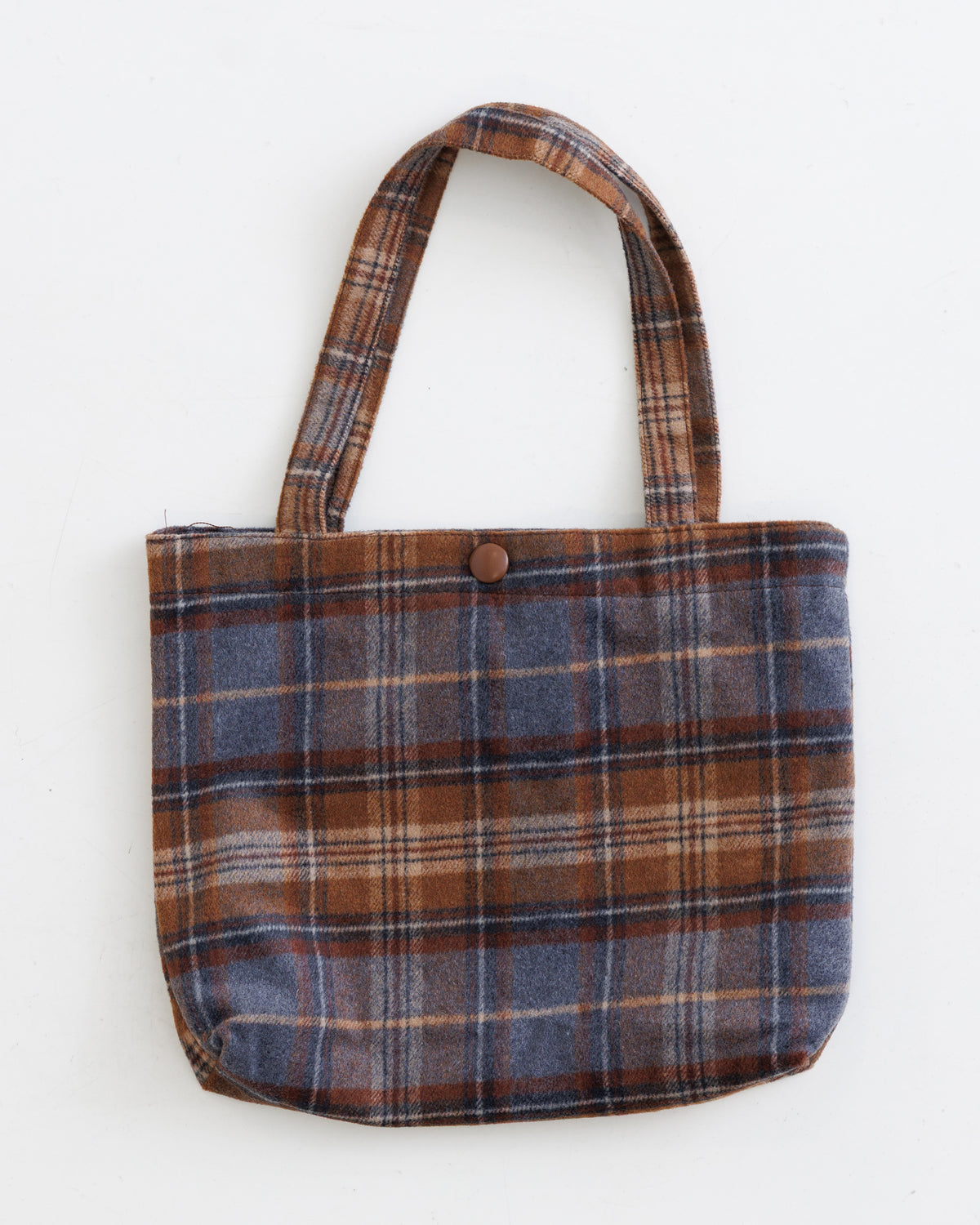 A small fabric tote bag with a brown, blue, and beige plaid pattern, featuring two shoulder straps and a single brown button closure at the top, shown against a plain white background.