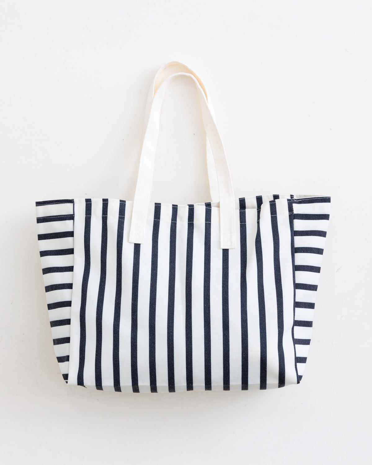 A canvas tote bag with vertical navy blue and white stripes, featuring two cream-colored fabric shoulder straps, photographed against a plain white background.