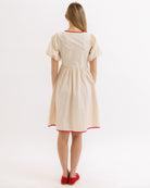 Woman wearing a beige dress with red trim on a white background