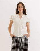 Woman wearing a white blouse and black checkered pants on a light background