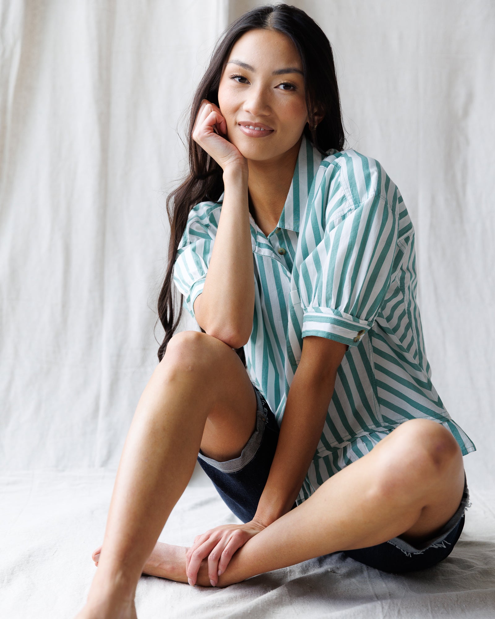 Woman wearing a striped shirt sitting on a bed with a white background