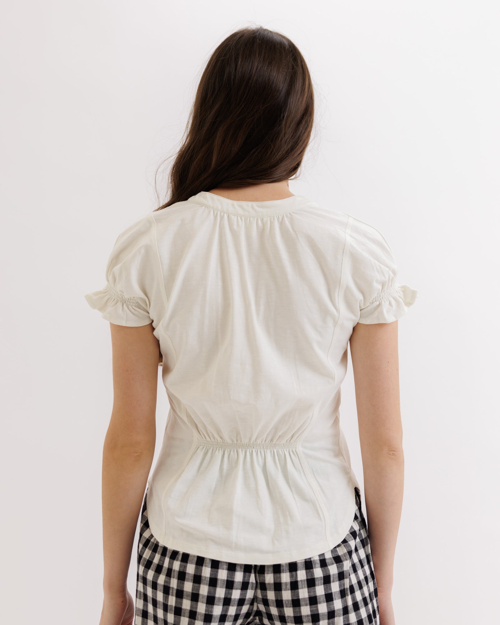 Person wearing a white blouse with ruffled sleeves on a plain background