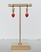 Gold hoop earrings with red coral drops on a gold stand against a light gray background