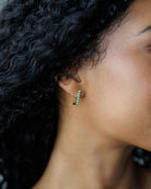 Close-up of an ear wearing a small earring with green gemstones.