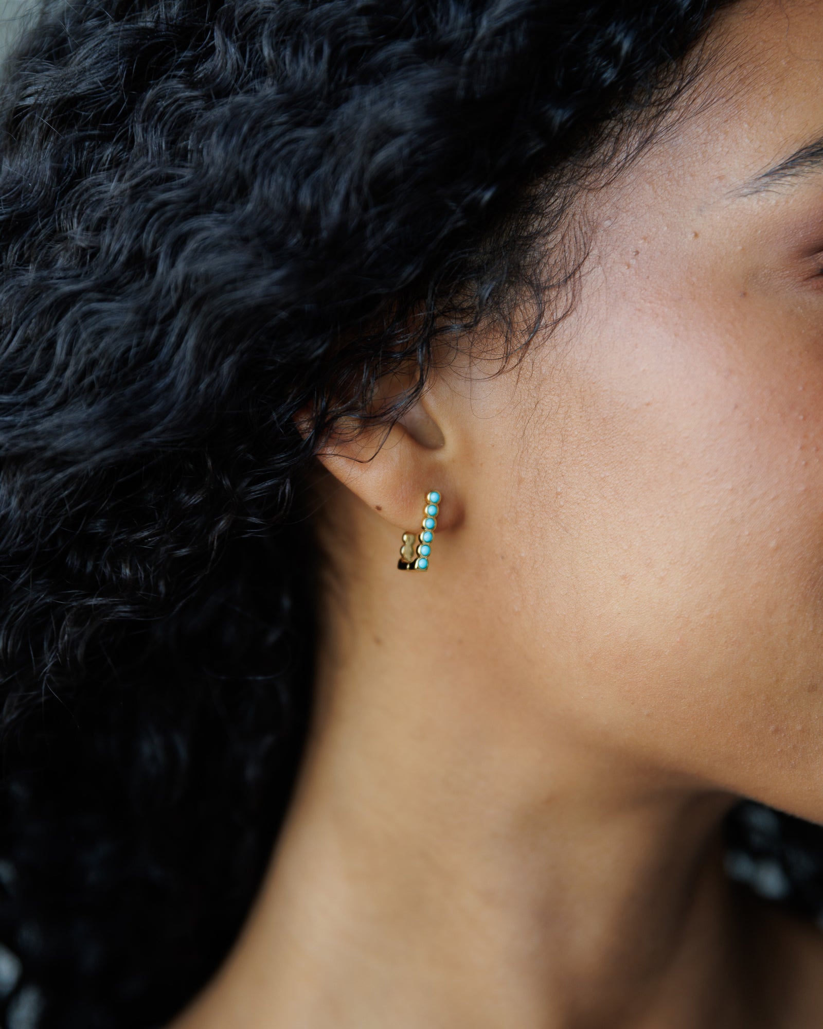 Close-up of an ear wearing a small earring with green gemstones.