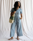 Woman wearing a blue checkered outfit holding a multicolored bag against a white background
