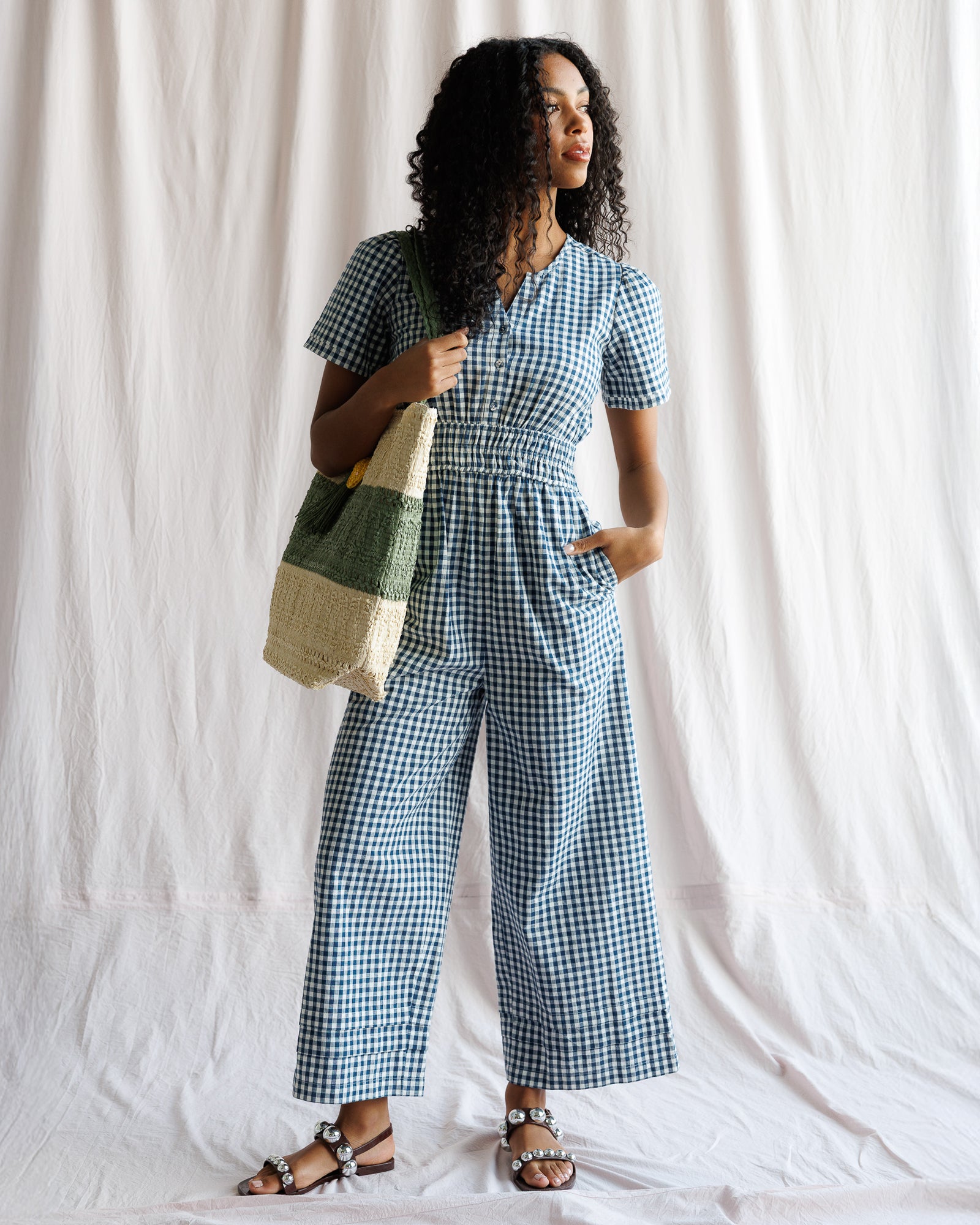 Woman wearing a blue checkered outfit holding a multicolored bag against a white background