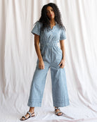 Woman wearing a blue and white checkered jumpsuit against a plain background