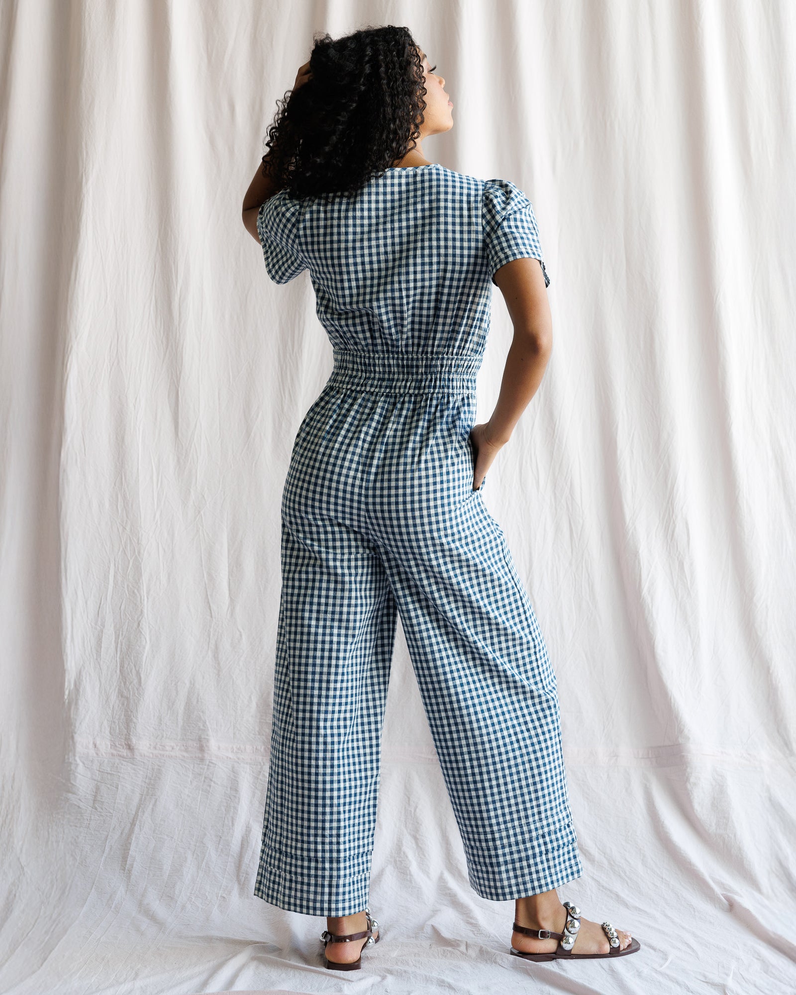 Woman wearing a blue and white checkered jumpsuit standing against a plain background