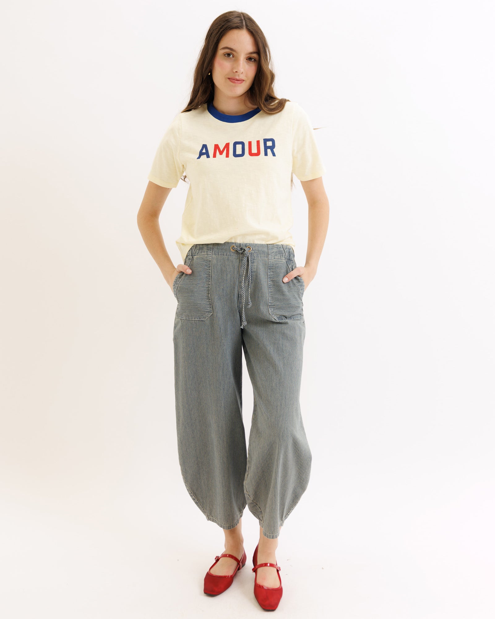 Woman wearing a cream t-shirt with 'AMOUR' text and gray pants on a white background