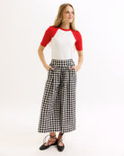 Woman wearing a red and white top with black and white checkered pants on a white background