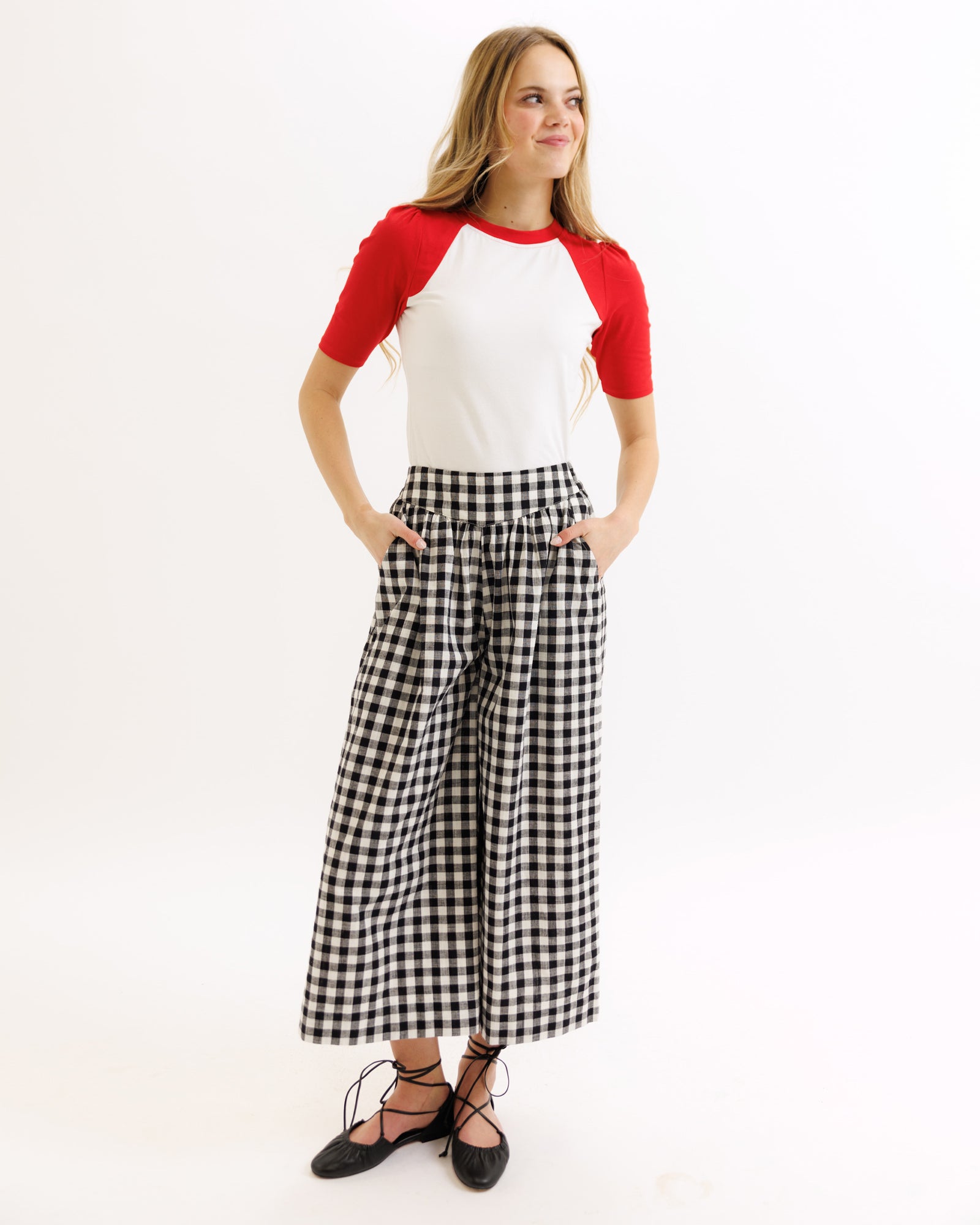 Woman wearing a red and white top with black and white checkered pants on a white background