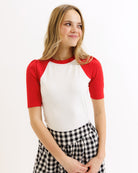 Woman wearing a red and white baseball shirt with a checkered skirt on a white background