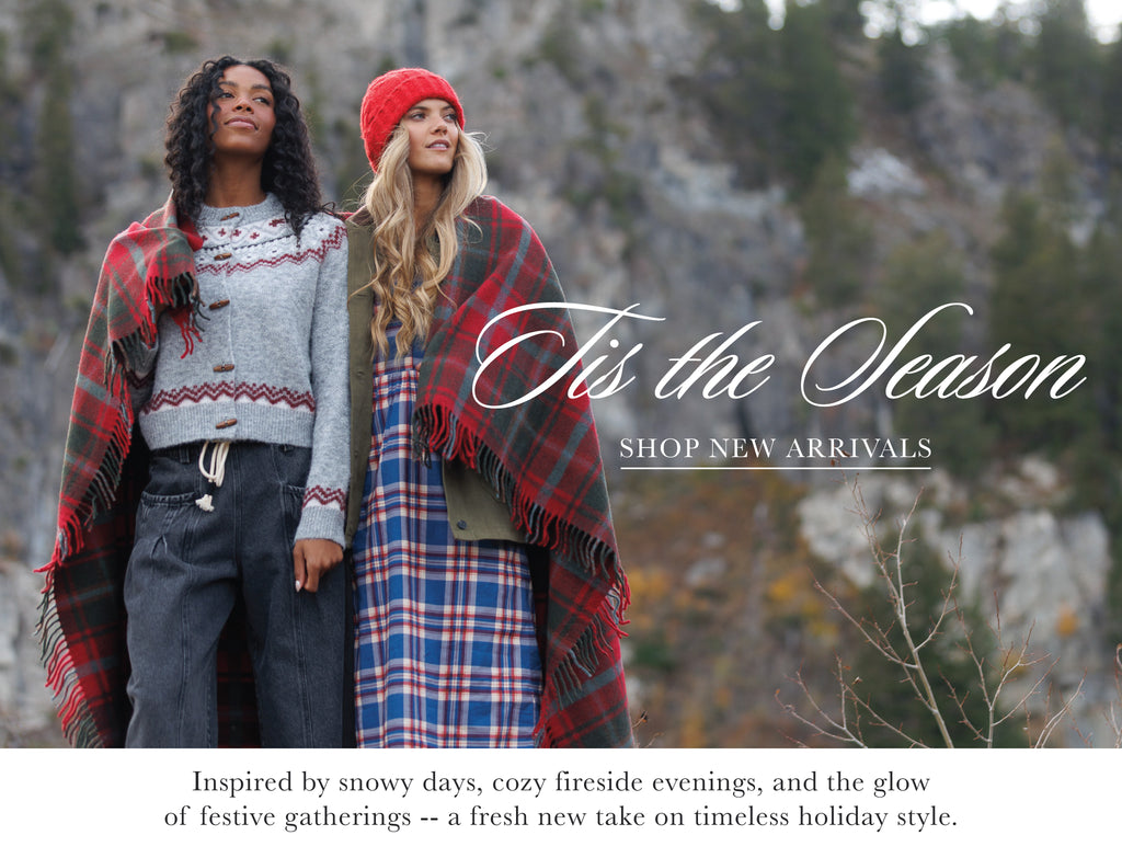 Two people wearing plaid blankets with a snowy landscape background and text overlay that says "'Tis the Season - Shop New Arrivals"