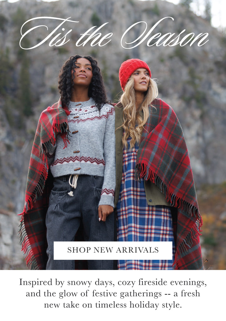 Two people wearing plaid blankets with a snowy landscape background and text overlay that says "'Tis the Season - Shop New Arrivals"