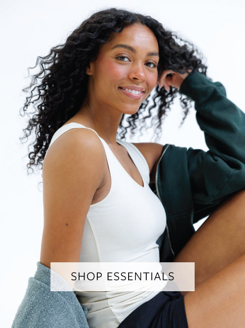 Woman in a white top and green sweatshirt with text 'Shop Essentials' on a white background