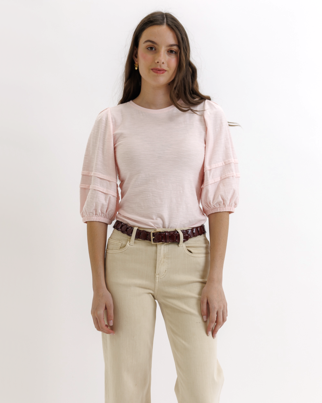 Woman wearing a light pink top and beige pants on a white background