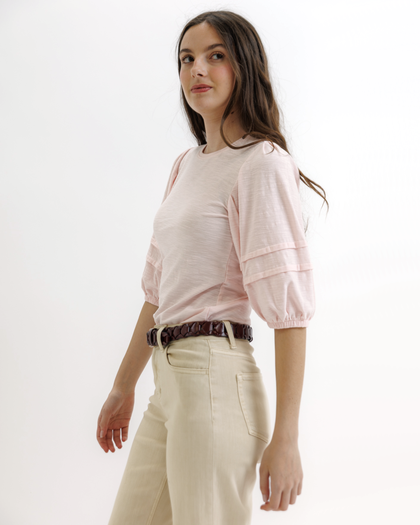 Woman wearing a light pink top and beige pants on a white background