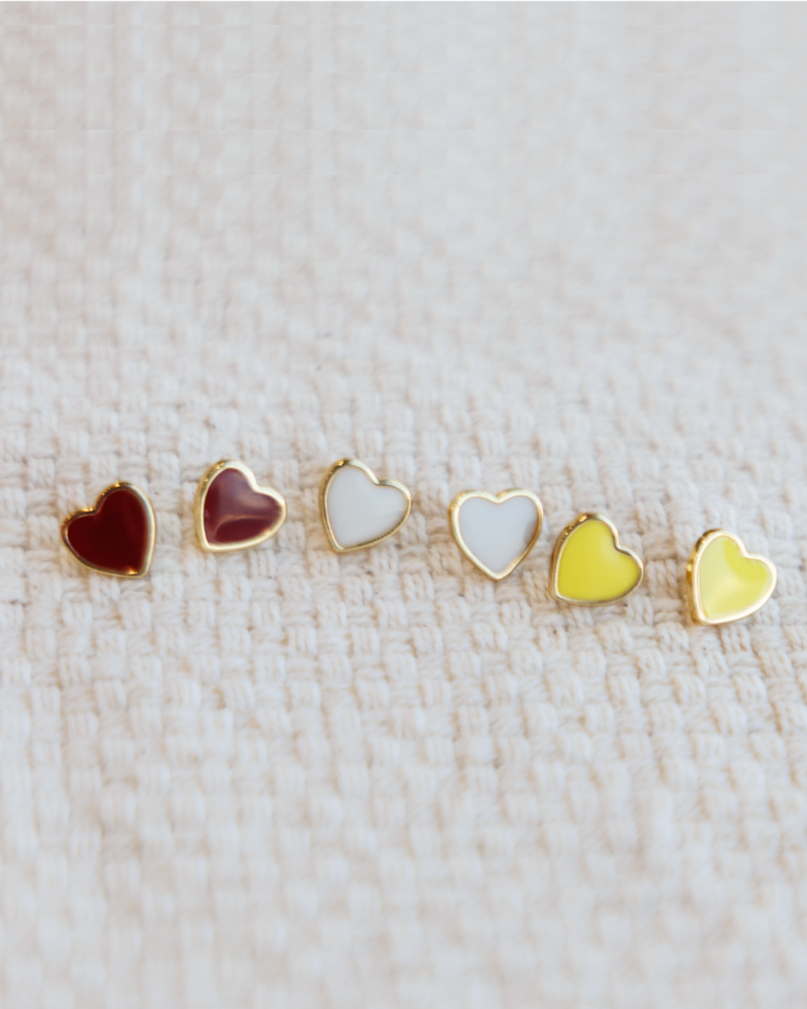 Set of heart-shaped earrings in various colors on a textured cream fabric
