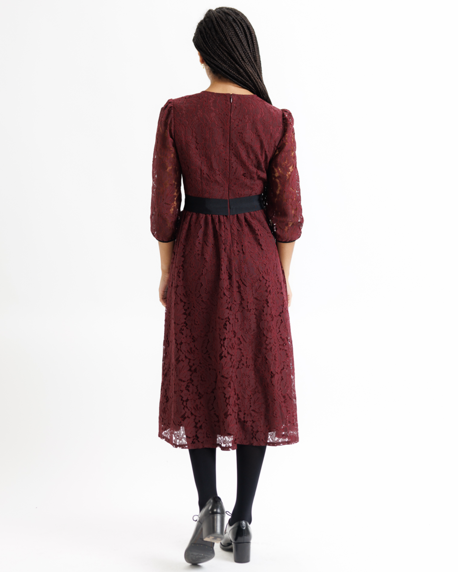 Woman wearing a burgundy lace dress with a black satin bow on a white background